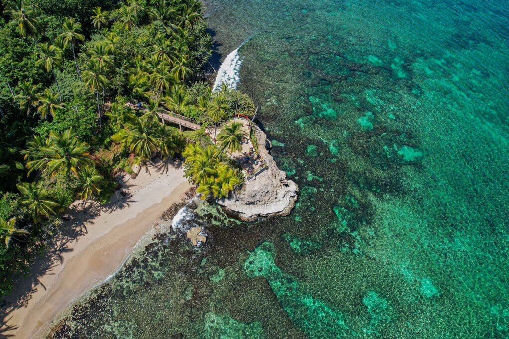 Aerial view of a tropical beach and turquoise Caribbean waters in Manzanillo near Puerto Viejo, Costa Rica, surrounded by lush rainforest and coral reef.