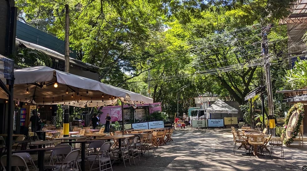 Shaded outdoor dining area in Medellín’s El Poblado neighborhood, with open-air seating surrounded by lush trees and local eateries.