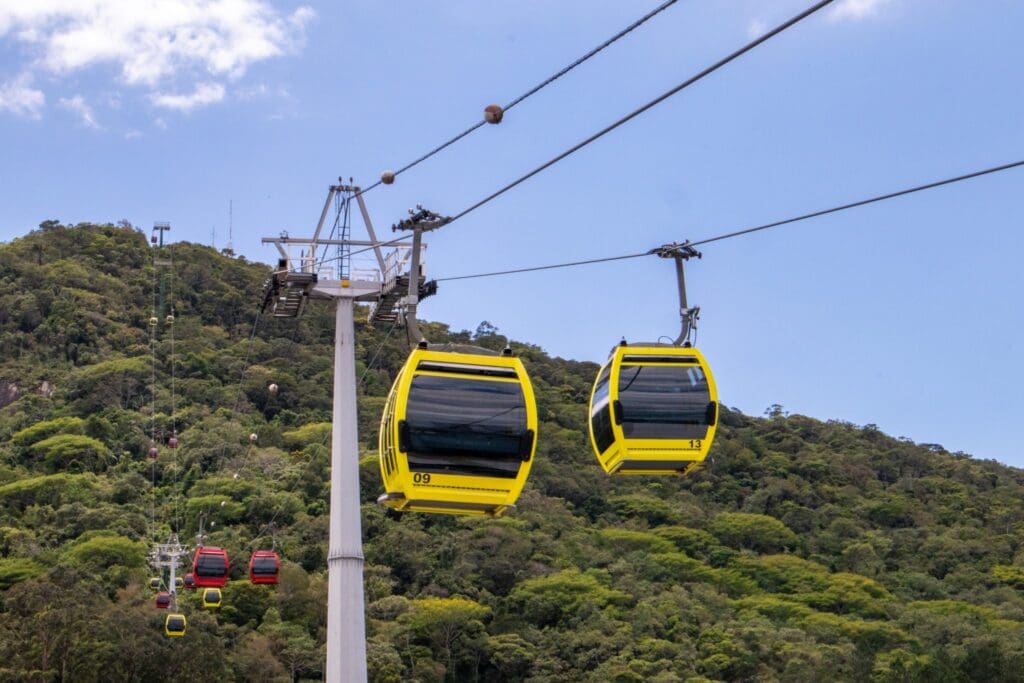 Bright yellow and red cable cars gliding over the green mountainside at Parque Arví in Medellín under a clear blue sky.